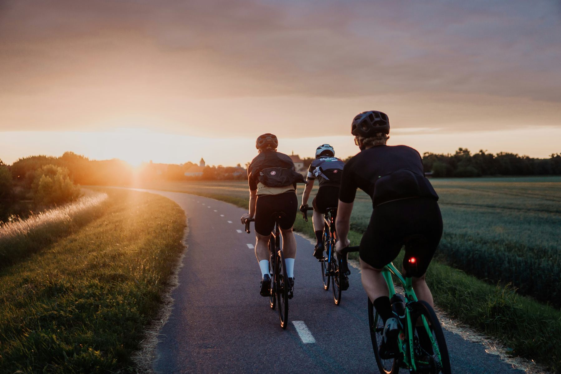 Drie racefietsers op een fietspad door velden bij zonsondergang